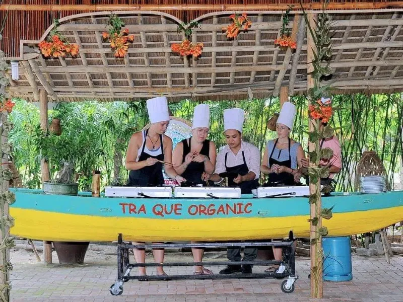 Explore Tra Que Vegetable Village in Hoi An: A Travel Guide to Vietnam’s Organic Farming Experience Visitors participating in a cooking class with local chefs using fresh vegetables from Tra Que Village, Hoi An